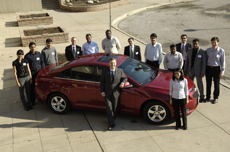 Dr Alpas with his past and present students standing around a new GM vehicle