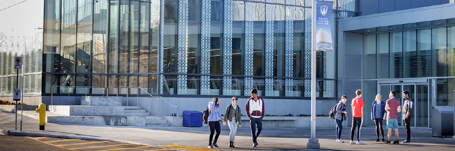 Three students smile while walking and talking outside of the University of Windsor's Toldo Lancer Centre.