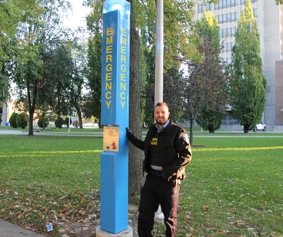 Campus Police Officer standing next to an emergency blue light pole