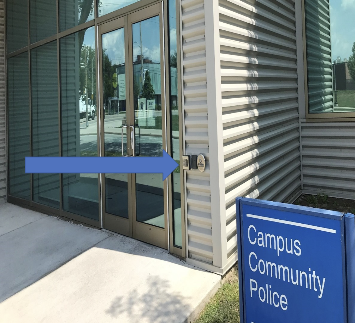 The main doors of the campus police office with a blue arrow pointing to the external speaker box.