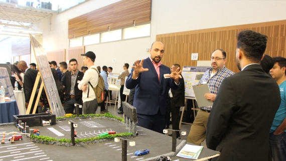 Habib Haider explains his group project, a system designed to reduce the impact of long lines waiting to access the Gordie Howe International Bridge, to professor Hanna Maoh of the Cross-Border Institute.