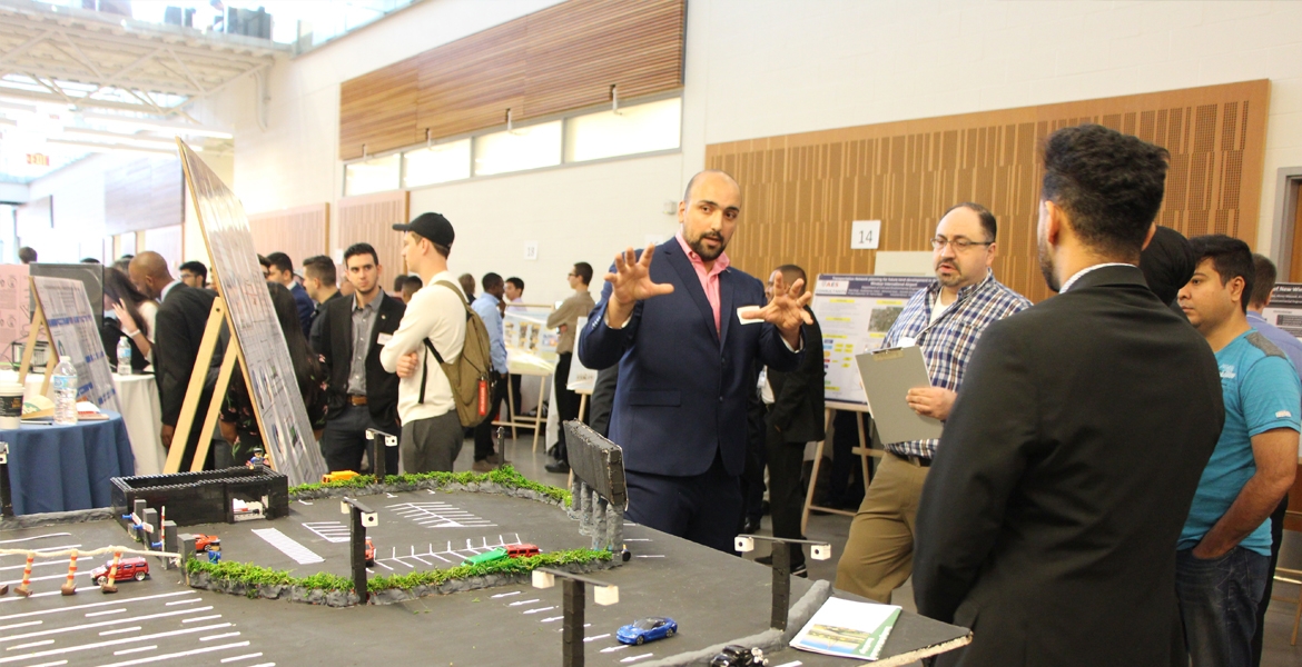 Habib Haider explains his group project, a system designed to reduce the impact of long lines waiting to access the Gordie Howe International Bridge, to professor Hanna Maoh of the Cross-Border Institute.