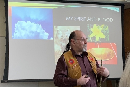 Elder Bryan Loucks speaks in front of a presentation of animal and plant pictures