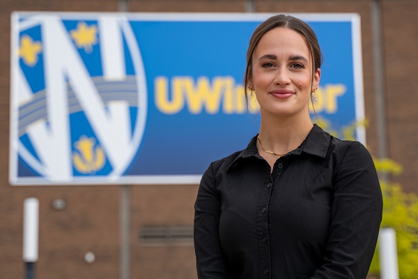 Meg Roberts standing in front of billboard displaying UWindsor shield