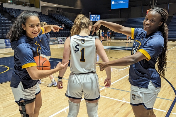 Isabella Anes, Teighan Stoukas, and Queenie Ndome display jersey reading $1