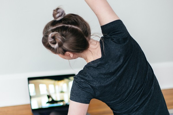 woman following yoga instructor on laptop