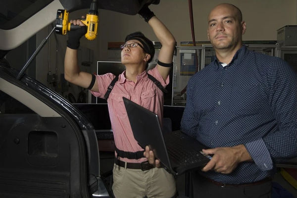 Xiaoxu Ji assembles a car, Joel Cort monitors his movements