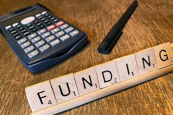 calculator, pen, Scrabble tiles spelling &quot;Funding&quot;