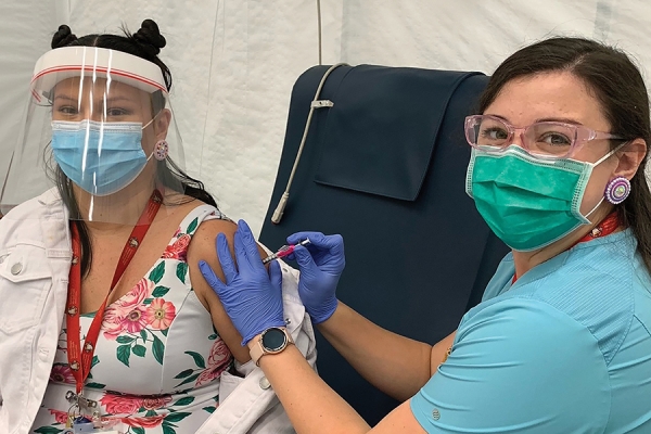 Nurse Sara Williams administers a vaccine injection to Lacey George -- both women wear masks