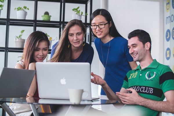 Group of young people have a discussion while sitting around computer.