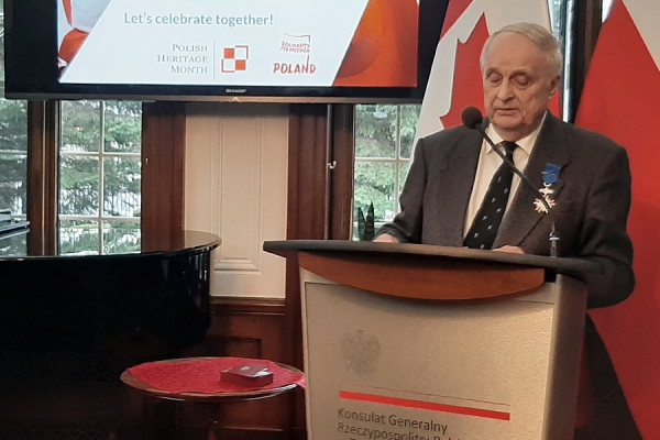 Frank Simpson at lectern with Polish flag behind