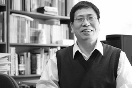 george zhou standing in front of a book shelf smiling