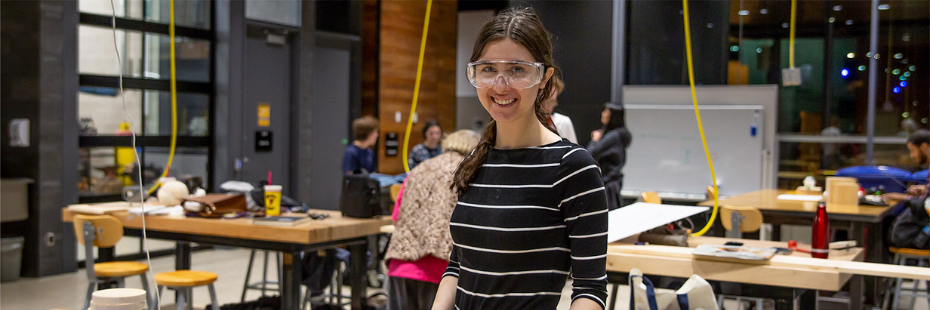 A female student standing in a workshop with safety glasses on