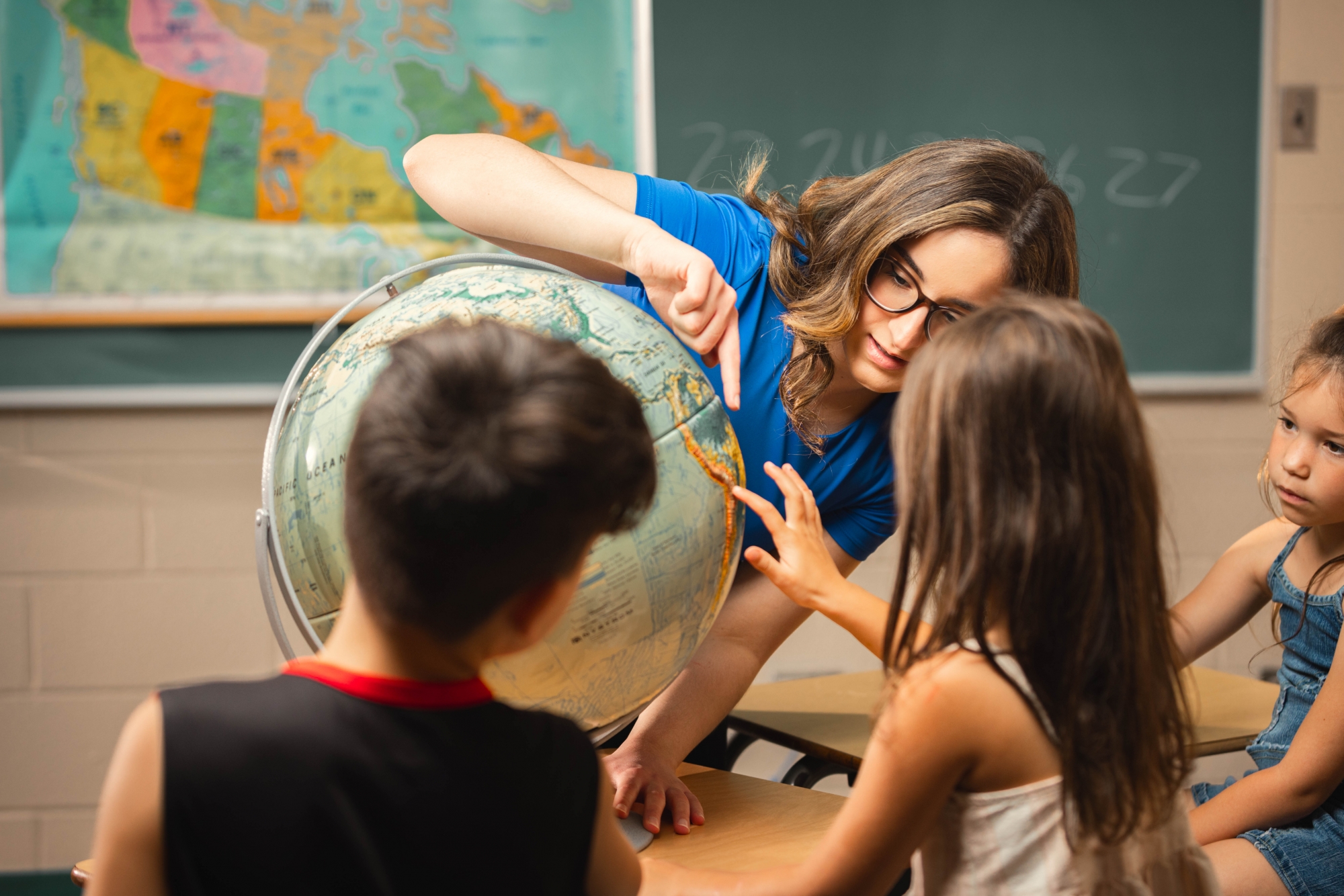 a teacher pointing at a globe with students watching