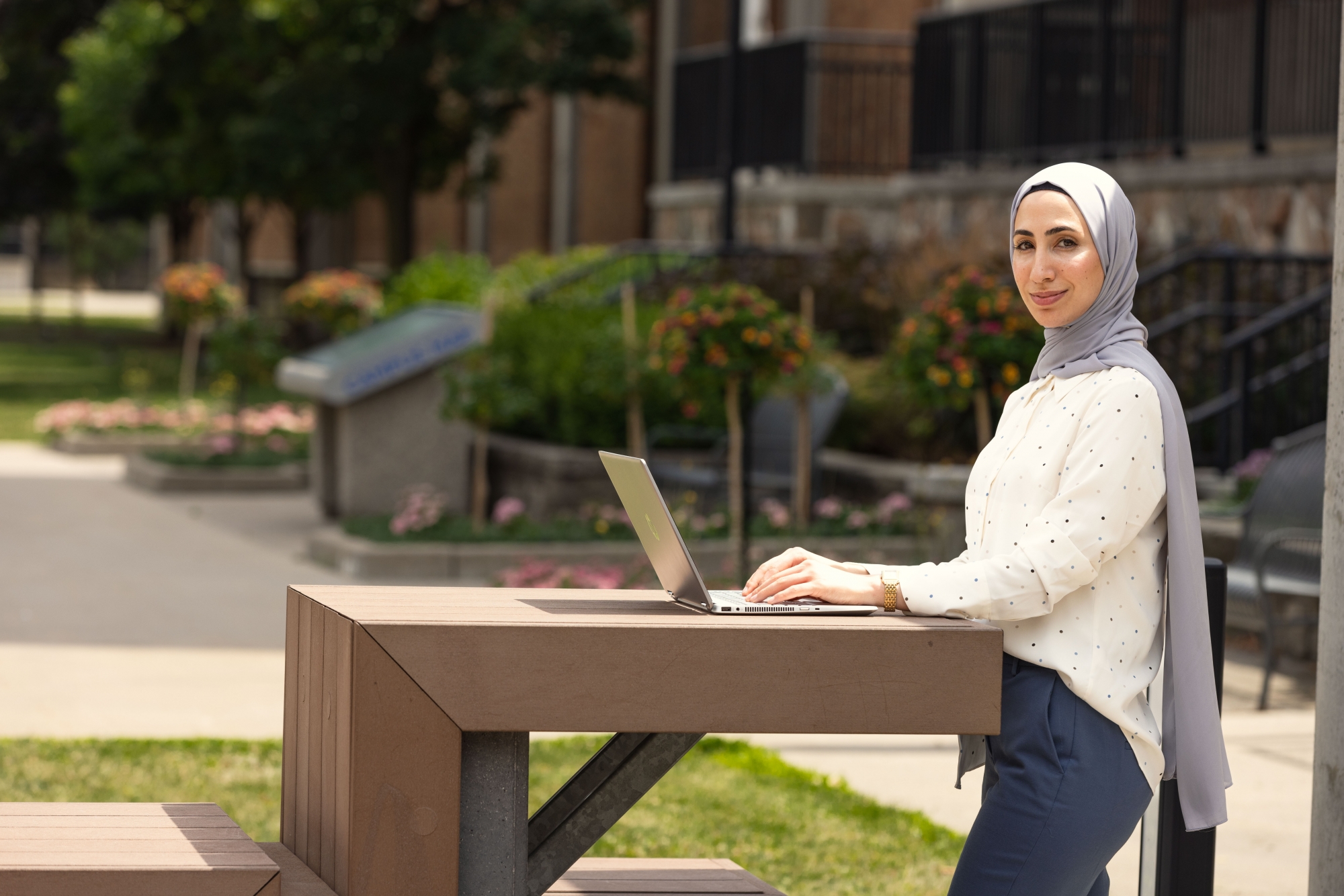 graduate student standing outside typing on a laptop