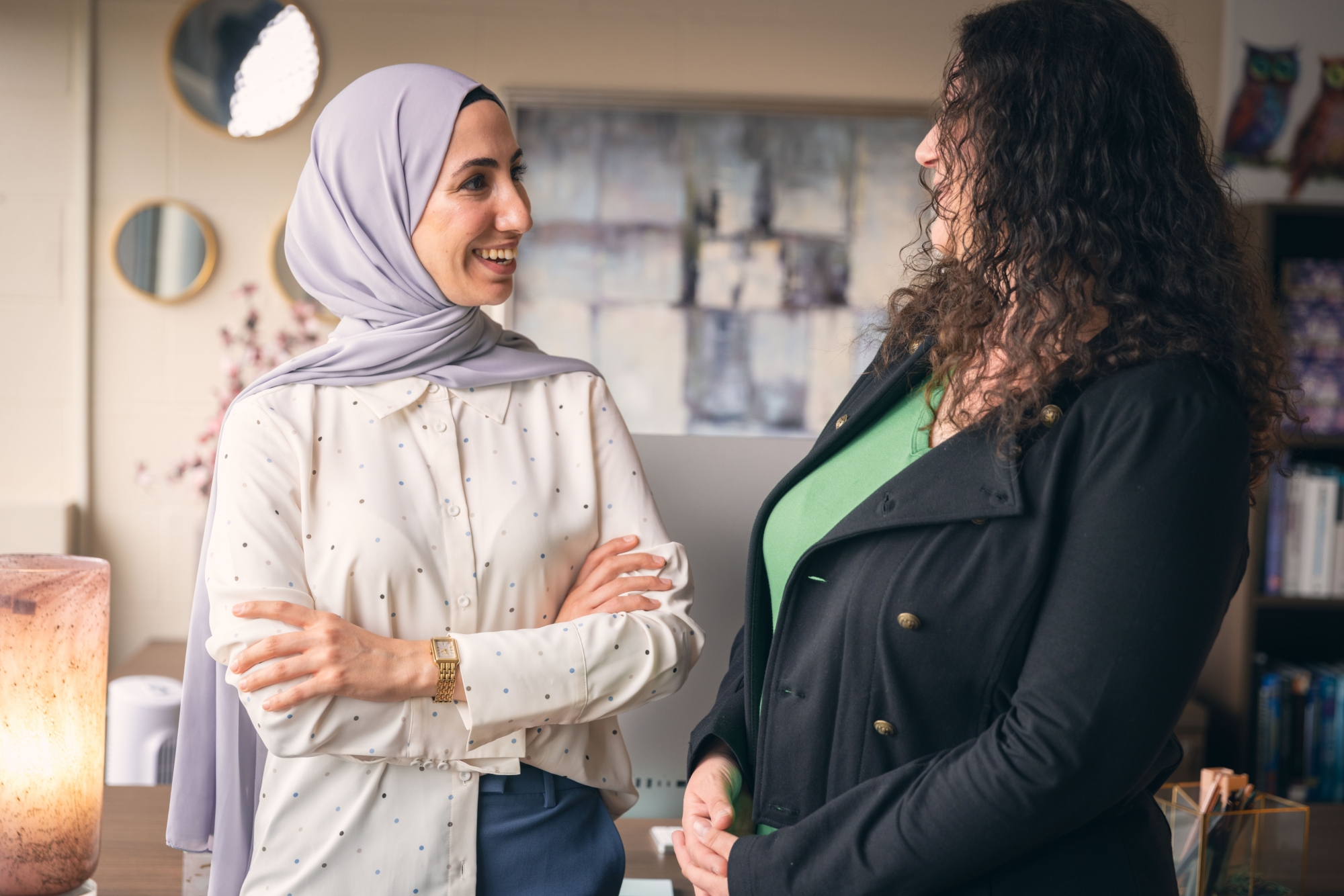 Two graduate students standing in an office smiling at each other. 