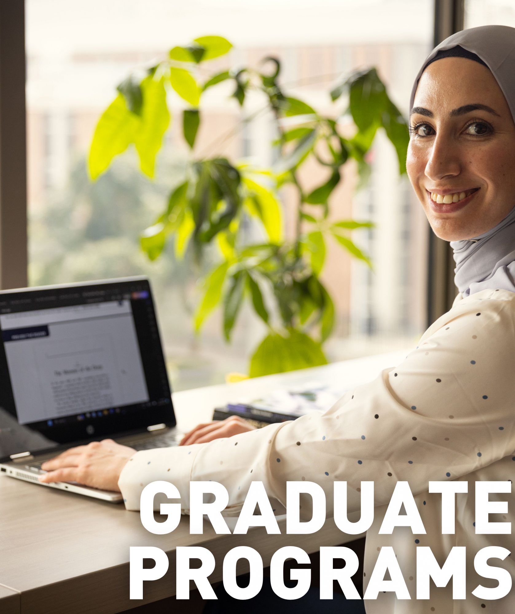 A Graduate student sitting at their laptop working on a research project.. The text "graduate" on the image