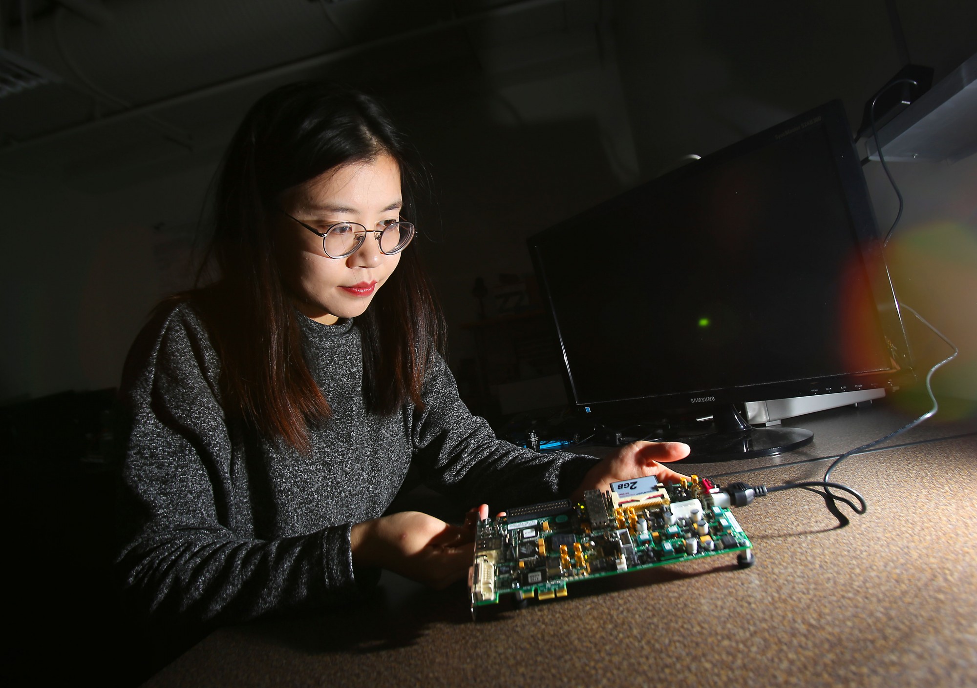 Meitong Pan, examines an FPGA board used to implement complex digital computations.