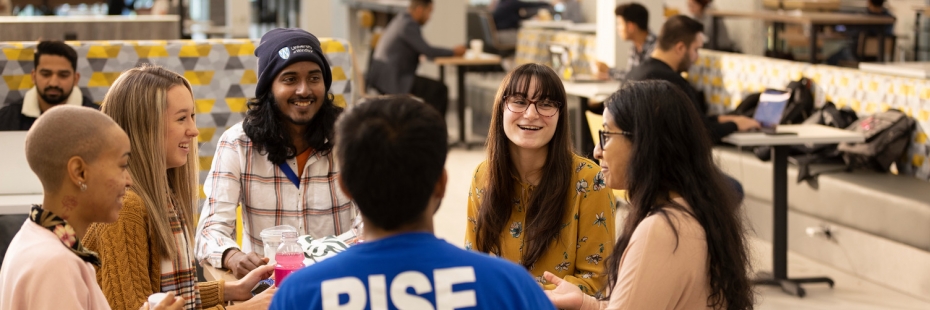 students sitting at a table conversing in caw centre.