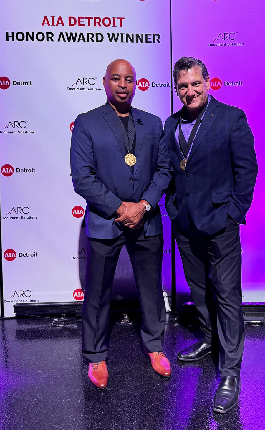 Photo of two men standing in front of a photo backdrop for the American Institute of Architects 