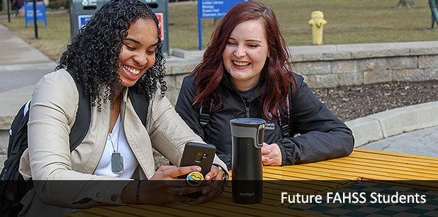 Two female students sitting at an outdoor table located outside of CAW Student Centre