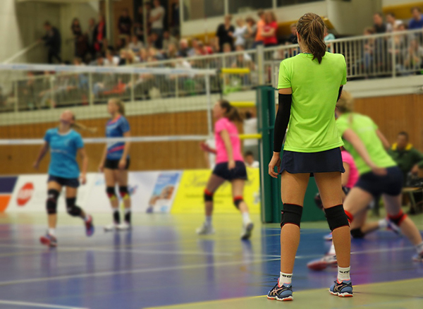 Women wearing bright coloured t-shirts play volleyball in a gym