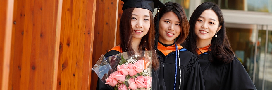 Three University of Windsor graduates hold a bouquet of flowers.