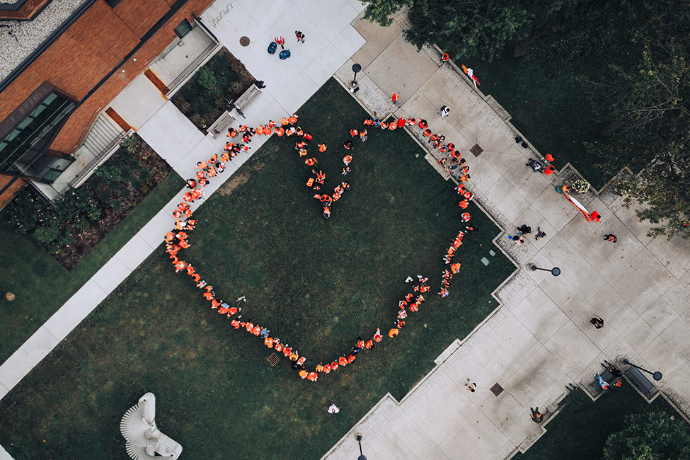 Overhead bird's eye view of people in orange shirts positioned in a heart shape