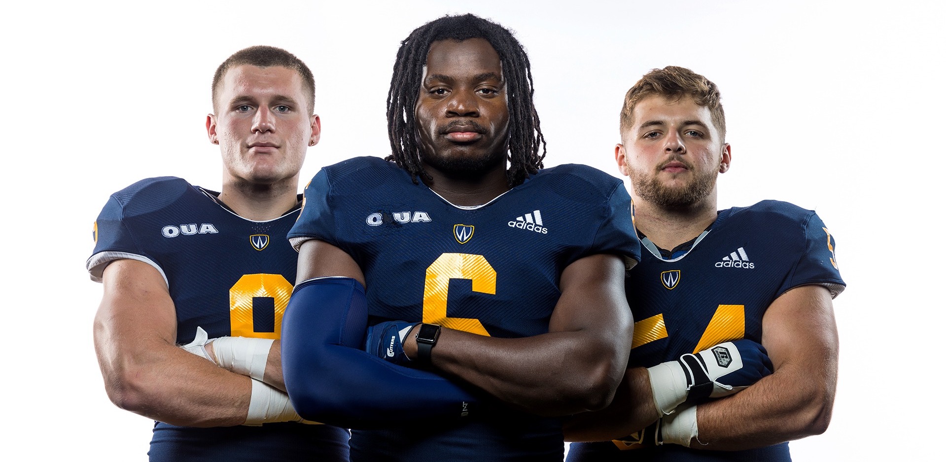 Three football players in uniform posing with their arms crossed