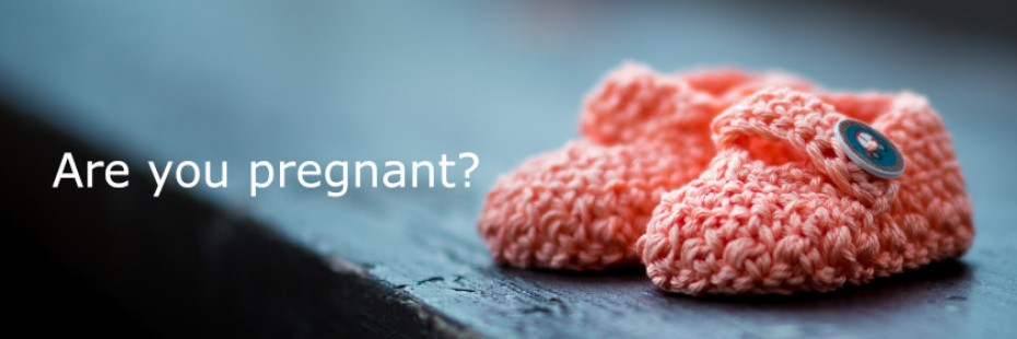 Knitted pink baby shoes on wooden table with the words Are you Pregnant?