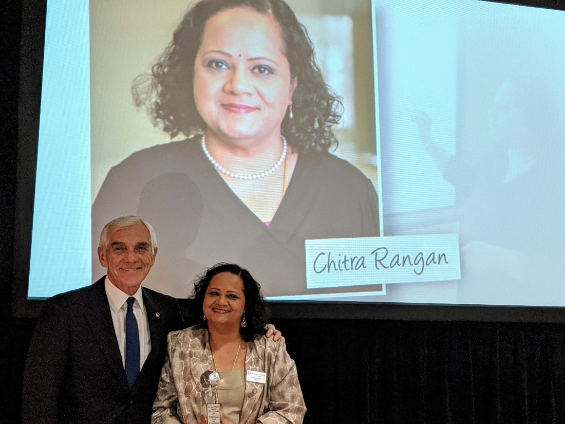 Dr. Chitra Rangan and Dr. Alan Wright with the 2019 Dr. Alan Wright award, in front of Chitra Rangan image on screen