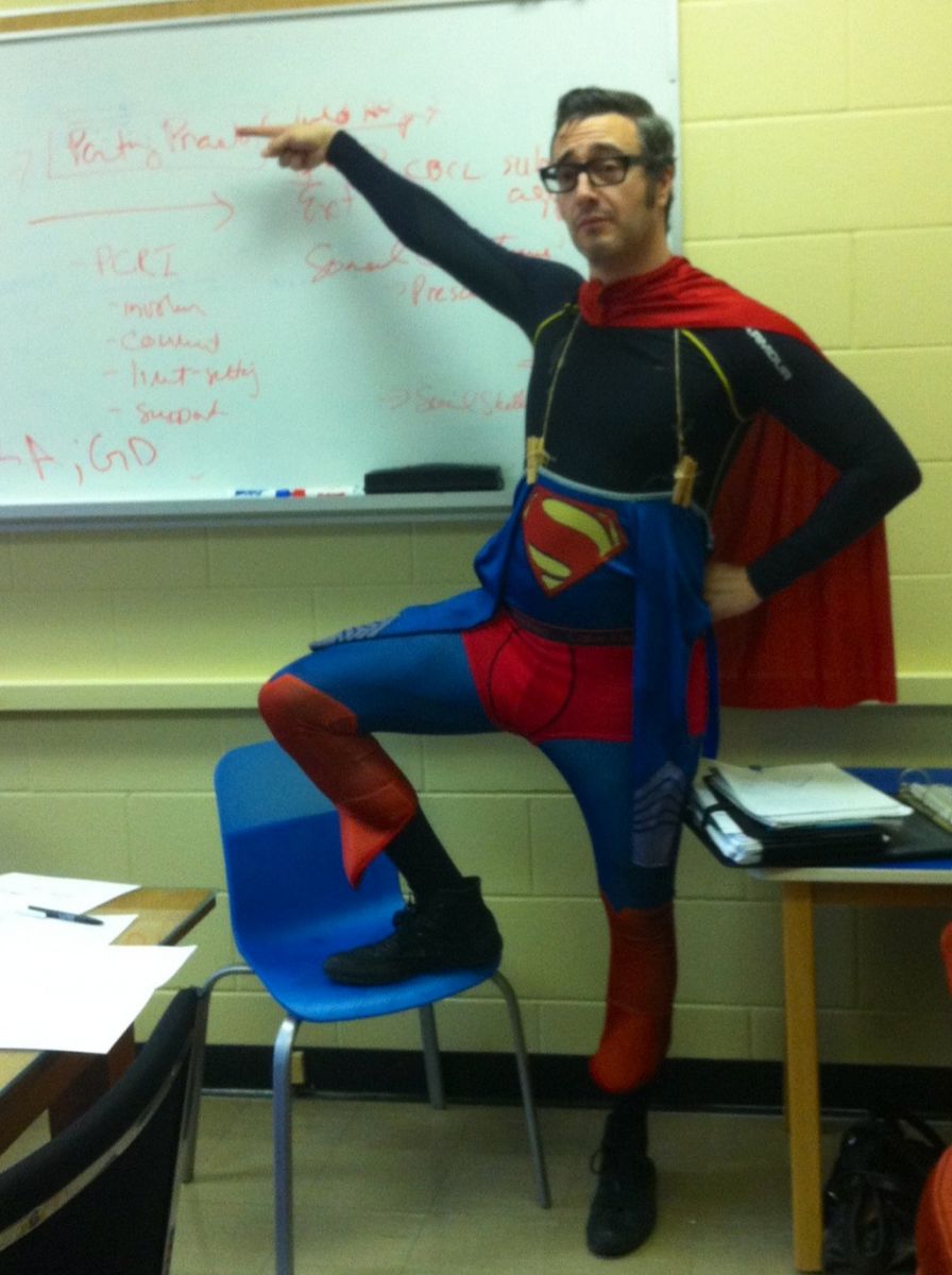 Dr. Pascual-Leone pointing at content on a whiteboard, wearing a Superman Halloween costume