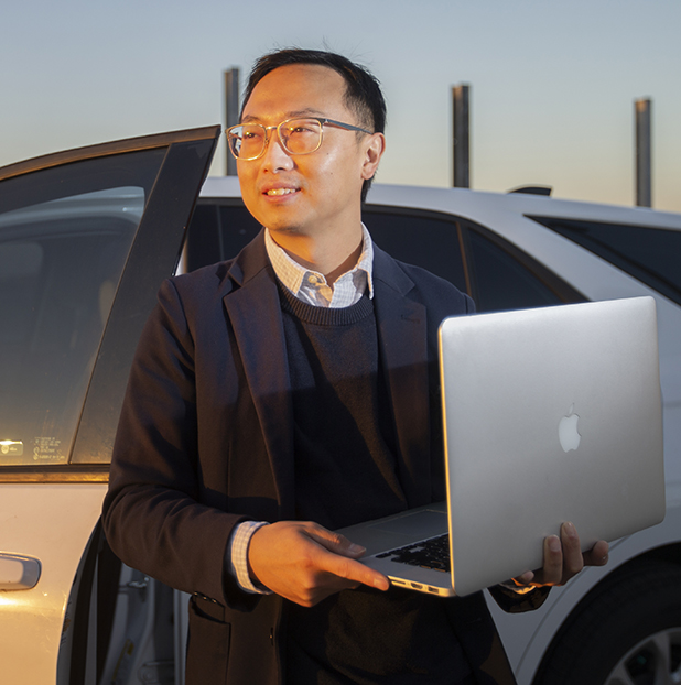 Ning Zhang holding computer outside car